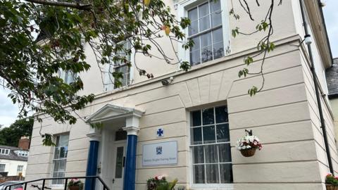 A white building with blue pillars around the front door, and a sign saying Banbury Heights Care 鶹Լ on the right hand side of the door