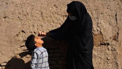 A burka-clad health worker administers polio vaccine drops to a child during a vaccination campaign in the old quarters of Herat in October 2020