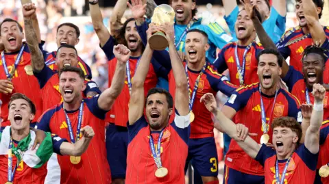 Rodri holds the World Cup trophy aloft as his Spain teammates celebrate with him