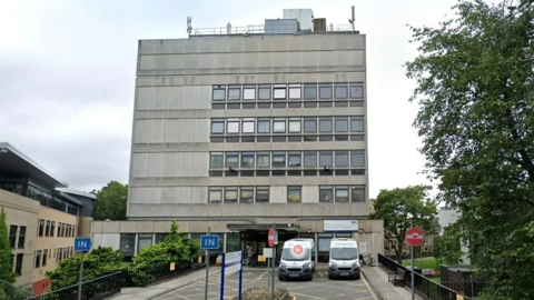 A grey building with five floors. Two ambulances are parked outside.
