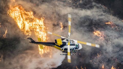 A helicopter flies over the wildfires.