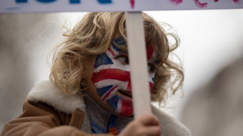 A child with a painted face holds a placard