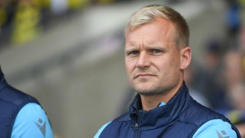 Oxford United boss Liam Manning looking serious in the dugout during a League One game.