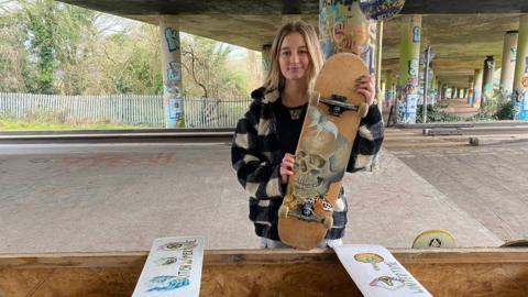 16 year old Ruby Parker holding up a skateboard featuring one of her painted designs