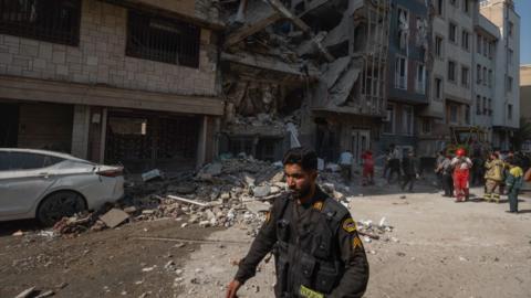 Iranian police officer walks past a damaged building in Tehran.