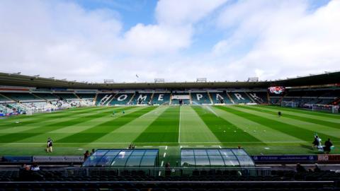 A general view of a football stadium interior. Players stand on a large green pitch. A Home Park sign is on display in one of the seating areas.