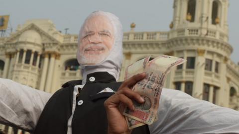 A man holds up 1000 rupee notes against a prop of Modi