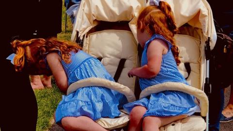Twin girls in matching blue dresses lean over to retrieve their snacks at the bottom of the buggy