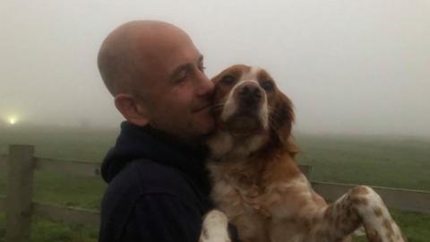 Man with bald head cuddles brown and white dog