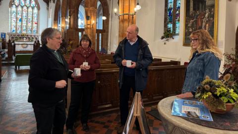 MP Ashley Fox is talking with three people inside a church. There are pews and the altar in the background.