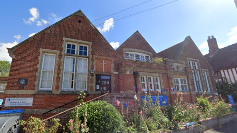 A general view of St Peter & St Paul Primary School. It is a red brick building with large windows. Blue, white and red bunting hangs on the front of the building.