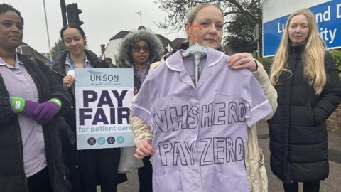 Lisa Smith holding a hospital uniform with the words "NHS HERE - PAY ZERO" written on it