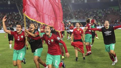 Morocco Women's Team celebrating on the pitch with the Moroccan flag during Afcon 2022.