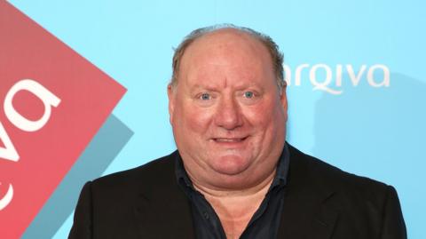A picture of Alan Brazil wearing a blazer and shirt.