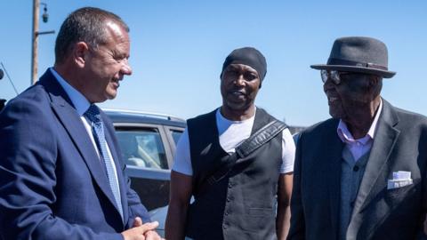 Paul Dale from the Port of Tilbury (left) welcoming artist Evewright (centre) and Windrush passenger Alford Gardner to Tilbury