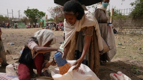 An aid worker distributes measured portions of yellow lentils to residents of Geha subcity