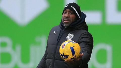 Port Vale manager Darren Moore holds the ball out in his left hand for a player to take a throw in during a match
