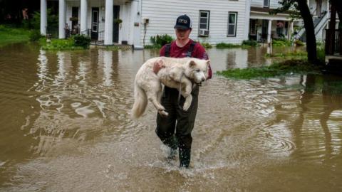 Tyler Jovic, of Montpelier, carries his neighbor's dog to dry ground on Tuesday afternoon,