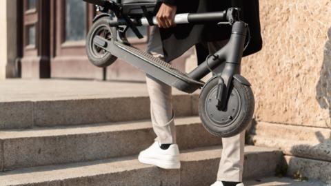 Unrecognizable young man carrying an electric push scooter up the stairs