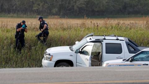 A Royal Canadian Mounted Police officer takes a pictures of police vehicles next to a pickup truck at the scene where suspect Myles Sanderson was arrested,