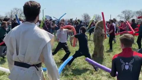 People fight with pool noodles in a park