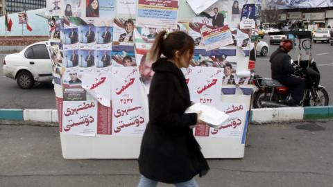 Women walk past posters of election candidates on a giant model ballot box in Tehran, Iran (28 February 2024)