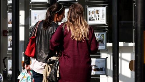 Two women look at houses in an estate agent's window