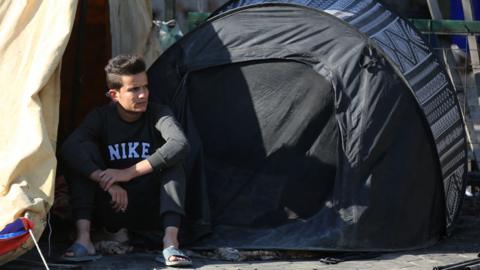 Man sits next to damaged tents at protest camp set up by supporters of Iran-backed Shia Muslim militias in Baghdad, Iraq (6 November 2021)