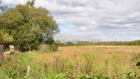 A visual representation of the Energy Recovery Facility at Chapel Gate Eco Park - a large grey boxy building - looking from across a field.