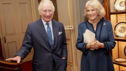 King Charles III smiling alongside Camilla, the Queen Consort