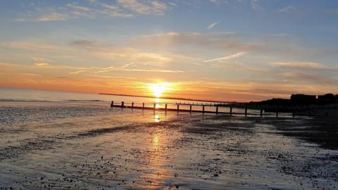 The sun rises in a bright yellow glow in a stripe of orange sky above a shoreline