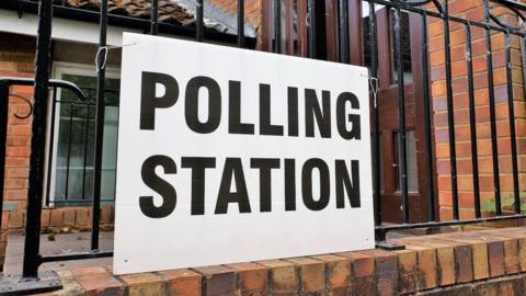 A polling station sign attached to railings outside a building