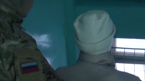 A screengrab of a video showing the woman wearing a white hat being escorted by a uniformed officer