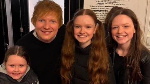 Ed Sheeran poses for a picture with Molly and Ruby Mulholland. On the left hand side is the girls younger sister Daisy. All are smiling at the camera.