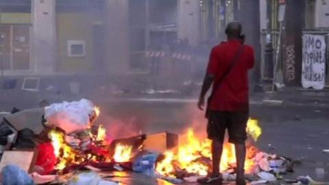 A man stands on a street beside rubbish and other items that have been set alight