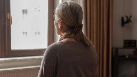 Senior woman sitting on bed and looking out of the window