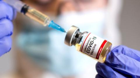 A woman holds a small bottle labelled "Covid-19 vaccine", 30 October 2020