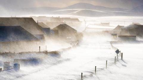 A wintry scene in Orkney with wind blowing snow across a road
