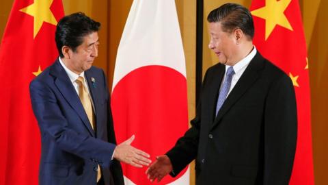 Japanese Prime Minister Shinzo Abe (R) shakes hands with Chinese President Xi Jinping