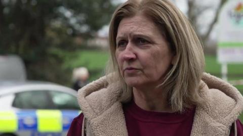 Alison Huntley owner and founder of Tigers Day Nurseries - she has blond hair and wears a dark red top with a light brown jacket - a police car is behind her.