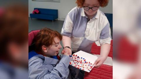 A volunteer helping a disabled child to paint.