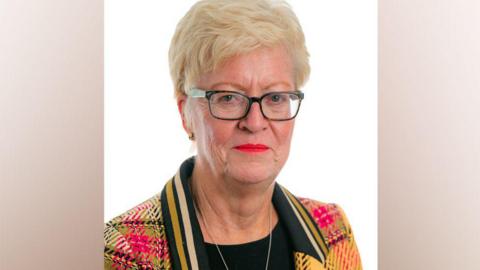 A headshot of Helen Pitcher, a blonde woman wearing glasses, red lipstick and an orange tartan jacket.