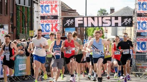 Runners taking part in the Chorley 10k with crowds lining the street to cheer them on. The race starts and finishes on Market Street with a black and white sign