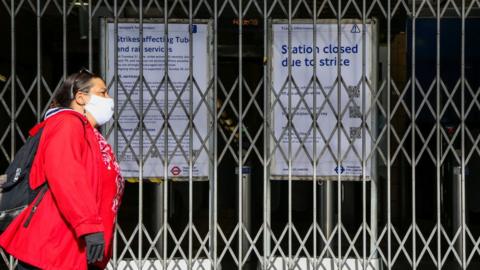 File photo showing woman walking past closed tube station entrance and strike notices in London.