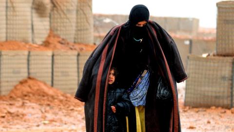 File photo: A Syrian refugee from the informal Rukban camp walks in the rain as she shelters a young child outside a UN-operated medical clinic, 1 March 2017