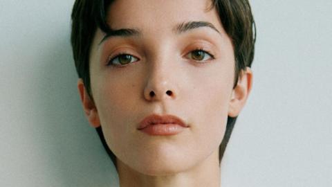 Jessica Reynolds, a woman with short, dark hair, looks to the camera with a neutral expression for a close-up photo. She has brown eyes and is lightly made up. 