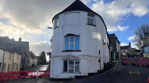 The top of St Nicholas Street street splits into two roads. There is a rounded three-storey building on the apex. Red barriers have been erected on both sides of the road to close off the area after the building was deemed to be unsafe by the emergency services.