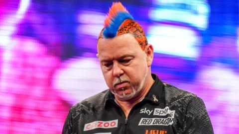 Peter Wright with a red and blue mohawk looks down