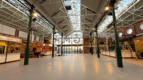 Bright, newly refurbished Goole Market Hall with a high glass roof, exposed dark green beams, and open floor space. Modern food‑stall units line the edges.