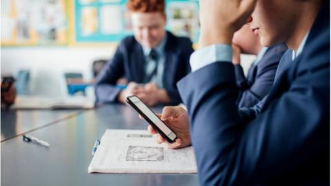 Pupils sitting at a table one with phone